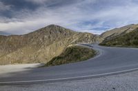 a motorcycle driving through a curve in the mountains next to a mountain road and mountain range