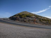 a curved road and mountain against a blue sky and a partly cloudy sky on the right