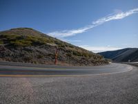 a curved road and mountain against a blue sky and a partly cloudy sky on the right