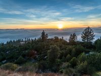 the sun sets behind the mountain range on the hill above the clouds on the horizon