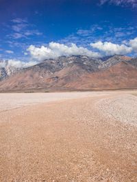 the desert has a brown substance and mountain in the background with snow on it and white clouds