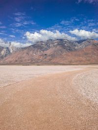 the desert has a brown substance and mountain in the background with snow on it and white clouds