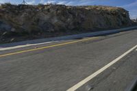 two people riding on a motorcycle down a mountainous road in the mountains near a hillside