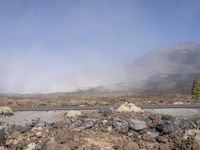 a road near the mountain side in the foggy sun day, and on the opposite bank are hills