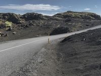 a motorcycle is driving down a mountain road in front of a few rocks and grass