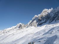 people are standing near a snow covered mountain side with skis in hand and one person has ski poles