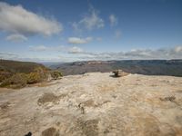 the mountain sits above and below an overcast blue sky with clouds, a lone man is on top of the rock