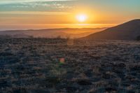 the sun sets on the hills over the horizon of the prairie in a fogy, mountainous country