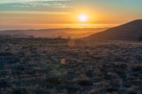 the sun sets on the hills over the horizon of the prairie in a fogy, mountainous country