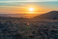 the sun sets on the hills over the horizon of the prairie in a fogy, mountainous country