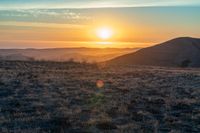 the sun sets on the hills over the horizon of the prairie in a fogy, mountainous country