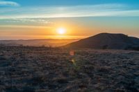 the sun sets on the hills over the horizon of the prairie in a fogy, mountainous country