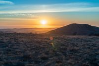 the sun sets on the hills over the horizon of the prairie in a fogy, mountainous country