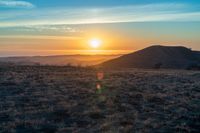 the sun sets on the hills over the horizon of the prairie in a fogy, mountainous country