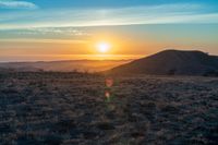 the sun sets on the hills over the horizon of the prairie in a fogy, mountainous country