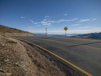 a road with yellow and white signs by the side of it on the road, in front of mountains