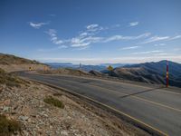 a road with yellow and white signs by the side of it on the road, in front of mountains