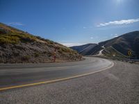 a lone highway on the edge of the mountain side under a clear blue sky with yellow line