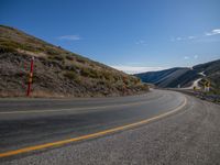 a lone highway on the edge of the mountain side under a clear blue sky with yellow line