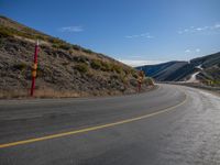 a lone highway on the edge of the mountain side under a clear blue sky with yellow line