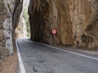a mountain road under a rock cliff next to a street sign that says no left turn