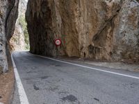 a mountain road under a rock cliff next to a street sign that says no left turn
