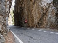 a mountain road under a rock cliff next to a street sign that says no left turn