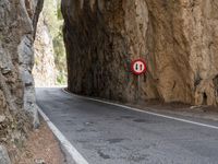 a mountain road under a rock cliff next to a street sign that says no left turn