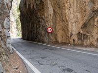a mountain road under a rock cliff next to a street sign that says no left turn