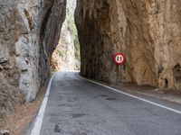 a mountain road under a rock cliff next to a street sign that says no left turn