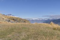 a field with some grass in it and mountains in the background with snow capped mountains