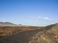 a lonely dirt road with a blue sky in the distance and a hill with small rocks and grass