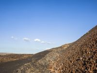 a lonely dirt road with a blue sky in the distance and a hill with small rocks and grass