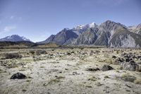 view from the top of mountain of sheep grazing in a barren plain below mountains with snow capped peaks