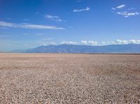 a person walking across a gravel field towards mountains in the distance, with a few trees on each end