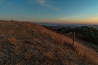 the sun rising over the mountains above the grass covered hills behind a fenced in area