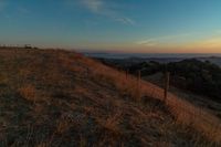 the sun rising over the mountains above the grass covered hills behind a fenced in area