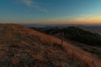 the sun rising over the mountains above the grass covered hills behind a fenced in area