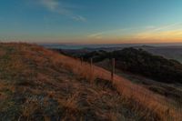 the sun rising over the mountains above the grass covered hills behind a fenced in area