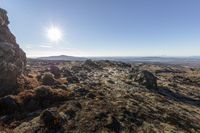 a rocky outcropping with the sun setting over mountains and hills in the distance