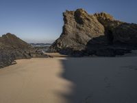 the sandy beach has a rock formation near it, as seen in this image from below