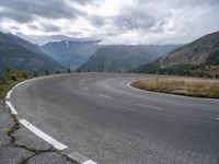 an empty, empty mountain road in front of a mountain range with some snow capped mountains behind