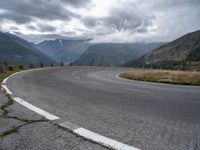 an empty, empty mountain road in front of a mountain range with some snow capped mountains behind