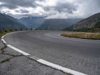 an empty, empty mountain road in front of a mountain range with some snow capped mountains behind