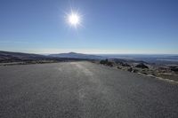 the sun is shining in the sky over a long road that winds through the mountain landscape