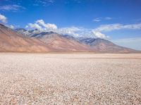 a field in a desert with mountains in the background with clouds and rocks and gravel