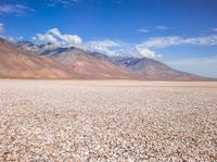 a field in a desert with mountains in the background with clouds and rocks and gravel