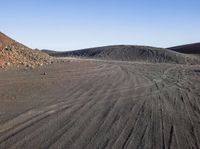 a gravel covered hill sits in the distance with no people in the background, with tire tracks visible