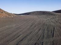 a gravel covered hill sits in the distance with no people in the background, with tire tracks visible