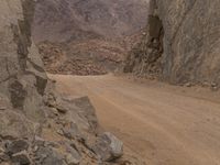 a small vehicle traveling across a barren road between some large rocks and boulders on one side